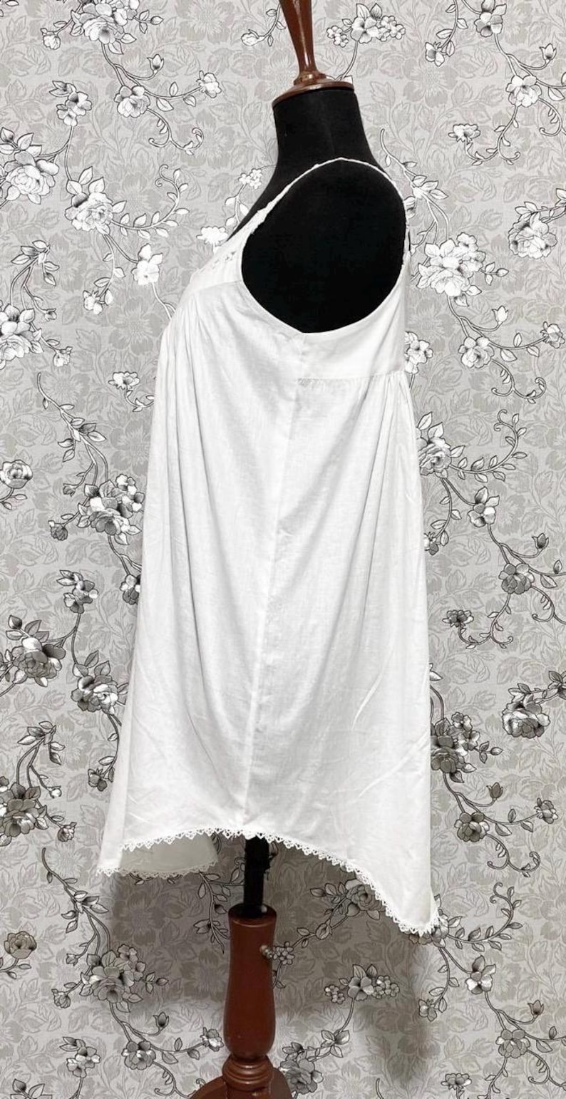 Peut inclure: Une robe de nuit blanche en coton avec une bordure en dentelle &agrave; l'ourlet. La robe est sans manches et a un col rond.
