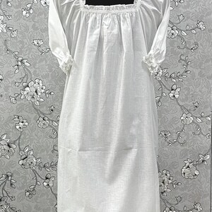 May include: A white, long-sleeved nightgown with a square neckline and ruffled cuffs. The dress features a gathered bodice and a knee-length hem. The fabric appears to be lightweight and breathable, suitable for sleepwear.