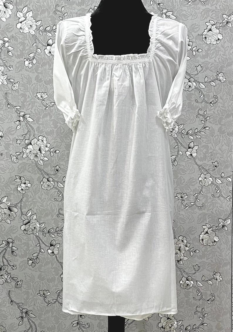 May include: A white, long-sleeved nightgown with a square neckline and ruffled cuffs. The dress features a gathered bodice and a knee-length hem. The fabric appears to be lightweight and breathable, suitable for sleepwear.