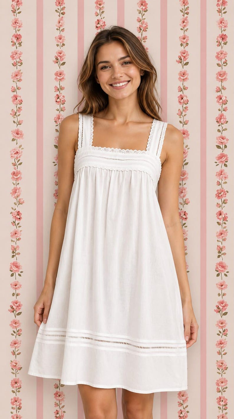 May include: A white sleeveless dress featuring a square neckline with delicate lace trim, a gathered bodice, and a horizontal lace insert detail near the hemline. The garment has a simple, loose-fitting silhouette and a clean, solid white color.
