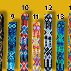 Op de afbeelding: Tien kleurrijke geweven vriendschapsarmbanden met de nummers 8 tot en met 14 gedrukt boven elk armband. De armbanden zijn gemaakt met verschillende kleuren en patronen, waaronder zwart, wit, rood, blauw, groen, geel en oranje.