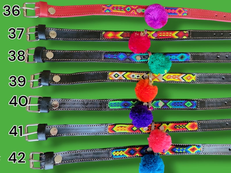 May include: A collection of seven leather belts numbered 36 through 42, featuring silver-toned metal buckles and colorful woven fabric inlays. Each belt is adorned with a single vibrant pom-pom in shades of purple, red, green, orange, or blue.