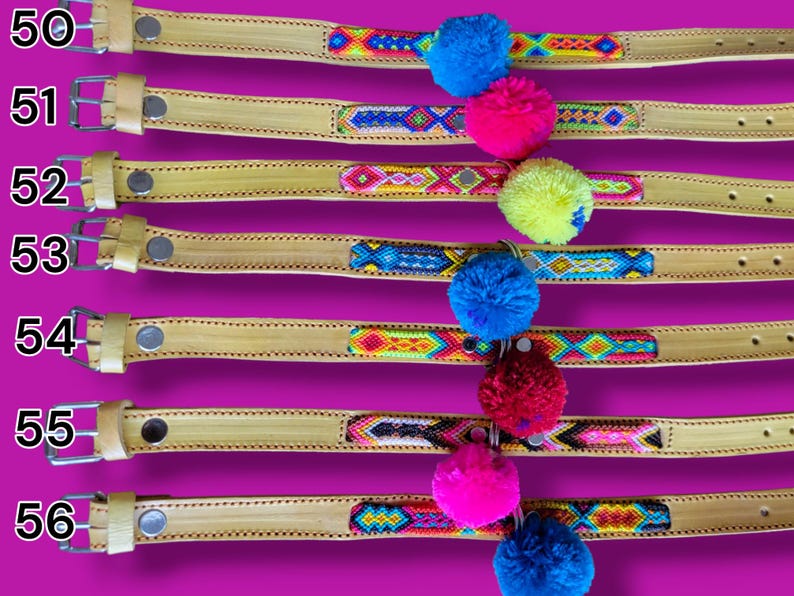 May include: Seven tan leather collars labeled 50 through 56, each featuring a central woven textile strip with geometric patterns in vibrant colors and a single large, fluffy pom-pom in blue, pink, yellow, or red attached to the center.