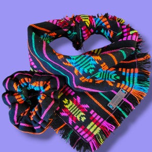 May include: A black bandana and matching scrunchie set with a vibrant, geometric pattern in shades of pink, orange, turquoise, and yellow. The bandana has fringed edges. The scrunchie is made of the same fabric.