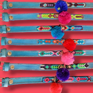 May include: Seven light blue leather collars numbered 22 through 28, each featuring a unique woven geometric pattern inlay and a single colorful pom-pom attached to a metal ring. Each collar includes a metal buckle and a gold-toned rivet.