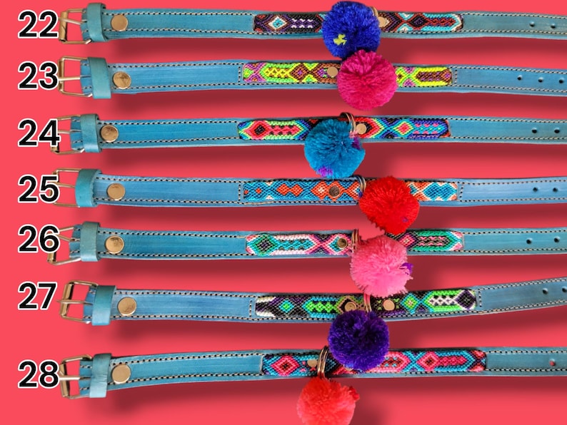May include: Seven light blue leather collars numbered 22 through 28, each featuring a unique woven geometric pattern inlay and a single colorful pom-pom attached to a metal ring. Each collar includes a metal buckle and a gold-toned rivet.