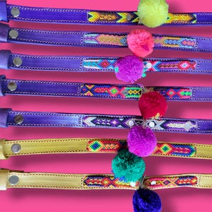 May include: Seven leather collars numbered 43 through 49, featuring vibrant woven patterns and colorful pom-poms. Collars 43 through 47 are purple, while 48 and 49 are yellow. Each includes a metal buckle, silver-tone hardware, and stitched edges.