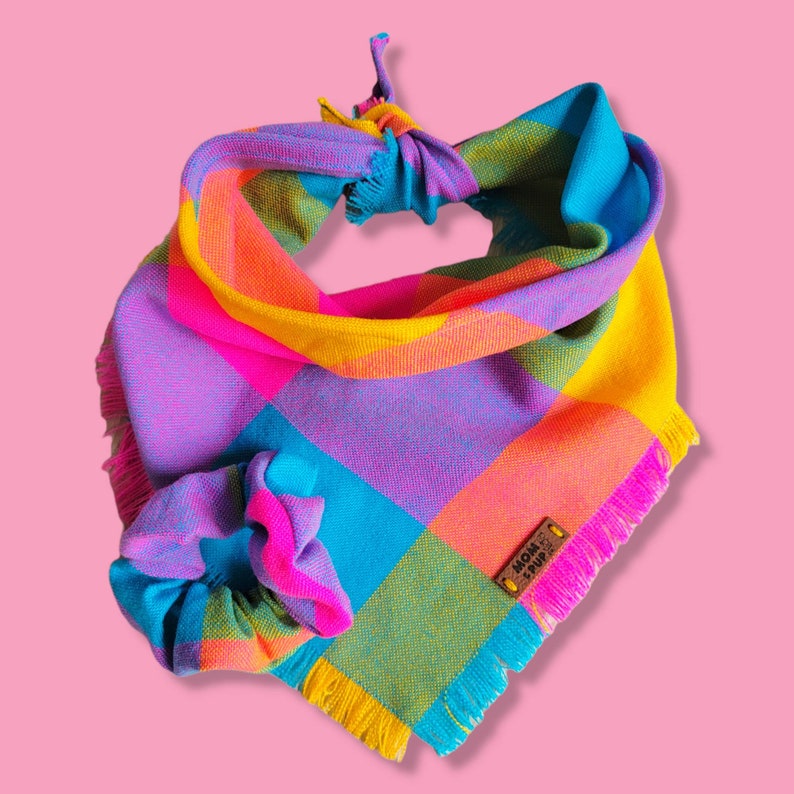 Puede incluir: Un pa&ntilde;uelo para perro colorido con un patr&oacute;n de cuadros rosa, amarillo, azul y verde. El pa&ntilde;uelo tiene un borde deshilachado y una etiqueta de cuero marr&oacute;n que dice "Mom & Pup".