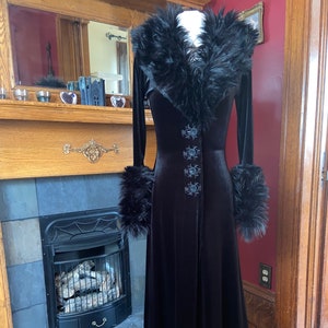 May include: A long black velvet robe with a faux fur collar and cuffs. The robe has a lace trim at the hem and features embroidered floral details.