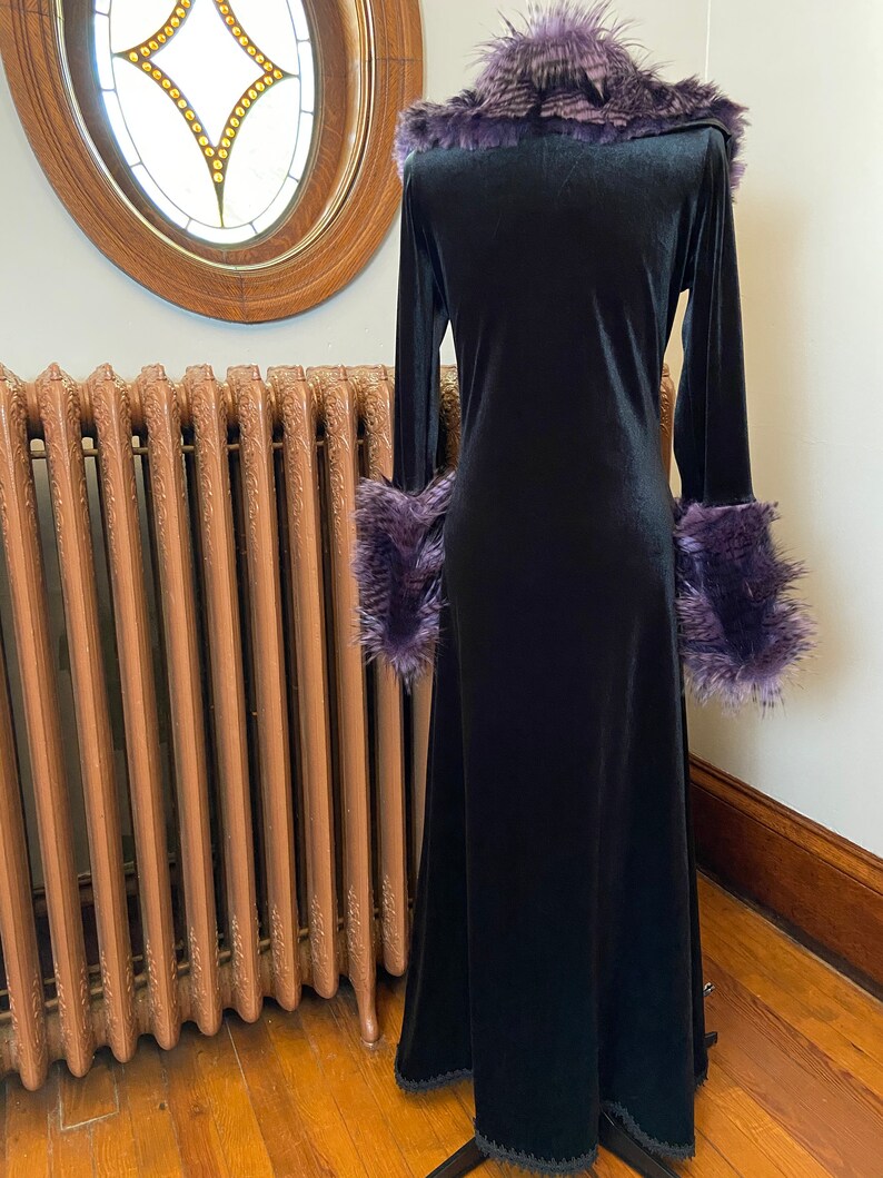 May include: A long black velvet robe with a purple faux fur collar and cuffs. The robe has a long, flowing skirt and a fitted bodice.