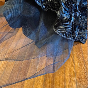 May include: A black tulle skirt with a layer of black satin fabric with a 3D rose design.