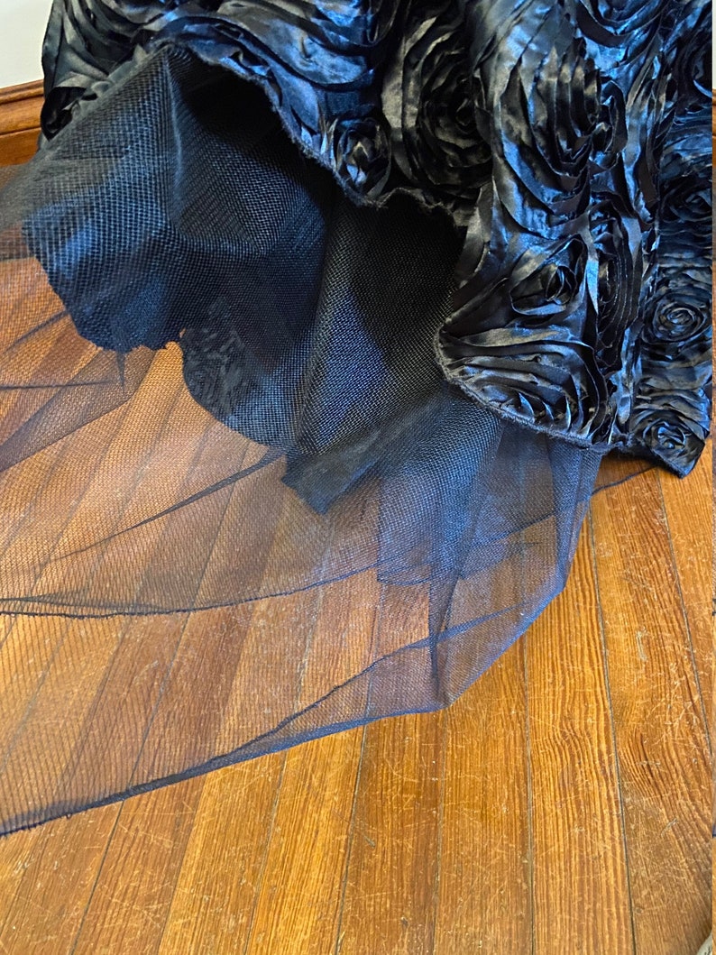 May include: A black tulle skirt with a layer of black satin fabric with a 3D rose design.
