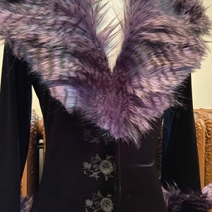 May include: A black velvet jacket with a purple faux fur collar and cuffs. The jacket has a button closure and embroidered floral details.