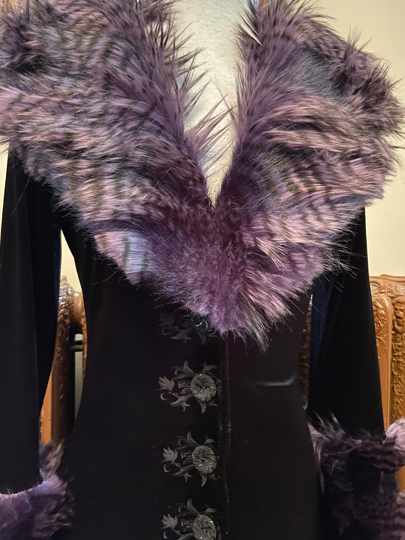 May include: A black velvet jacket with a purple faux fur collar and cuffs. The jacket has a button closure and embroidered floral details.