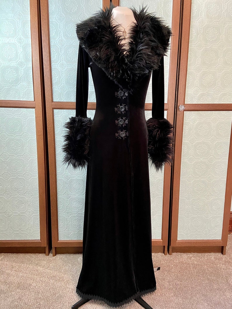 May include: A long black velvet robe with a faux fur collar and cuffs. The robe has a button closure and a lace trim at the hem.