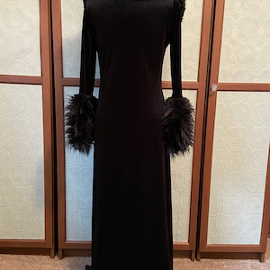 May include: A long black velvet robe with a faux fur collar and cuffs. The robe has a long, flowing silhouette and a simple design.