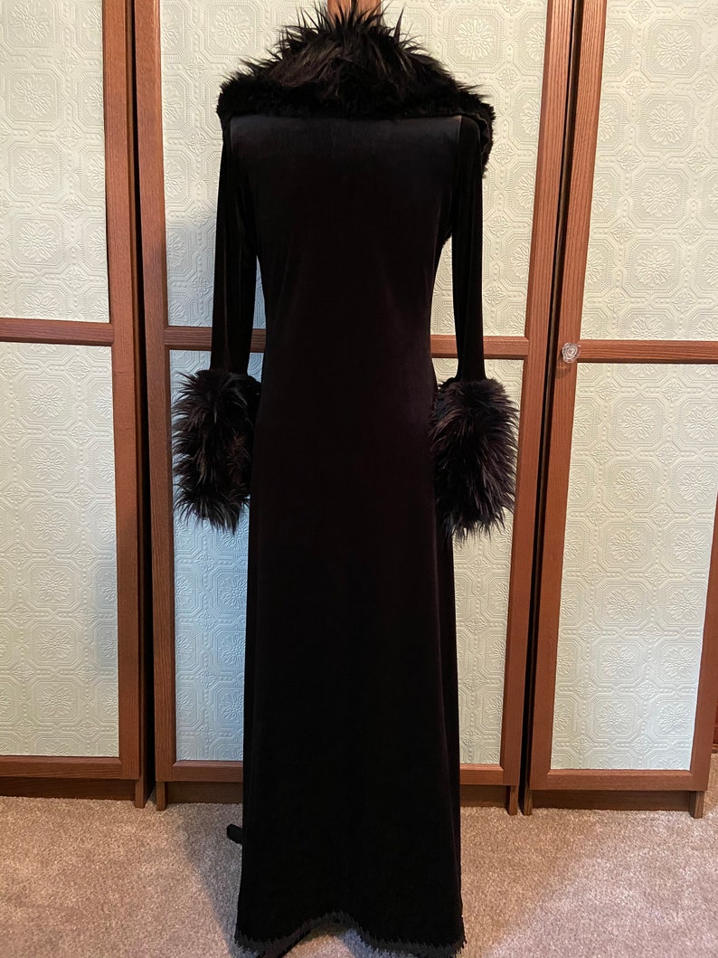 May include: A long black velvet robe with a faux fur collar and cuffs. The robe has a long, flowing silhouette and a simple design.