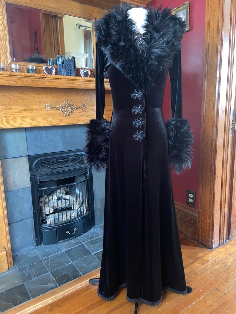 May include: A long black velvet robe with a faux fur collar and cuffs. The robe has a lace trim at the hem and features embroidered floral details.