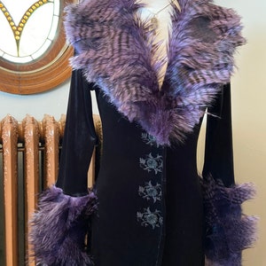 May include: A long black velvet coat with a purple faux fur collar and cuffs. The coat has a button closure and floral embroidery.