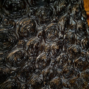 May include: Black fabric with a 3D rose pattern. The fabric is made of a soft, silky material and has a luxurious feel.