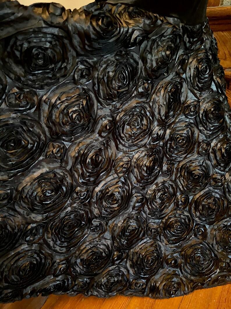 May include: Black fabric with a 3D rose pattern. The fabric is made of a soft, silky material and has a luxurious feel.