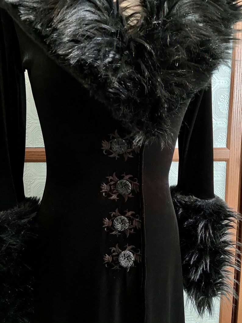 May include: A black velvet dress with a faux fur collar and cuffs. The dress has three decorative buttons down the front, each with a floral design.