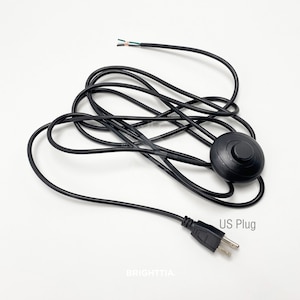 May include: Black foot pedal switch with a black cord and a UK plug. The cord is coiled and the switch is round with a black button in the centre.