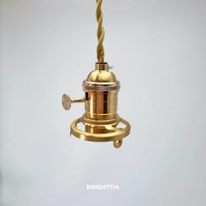 Peut inclure: Une douille de lampe de couleur laiton avec une base d&eacute;corative et un cordon torsad&eacute;. La douille a un petit levier et est con&ccedil;ue pour une ampoule de style Edison. Le mot "BRIGHTTIA" est imprim&eacute; en bas.