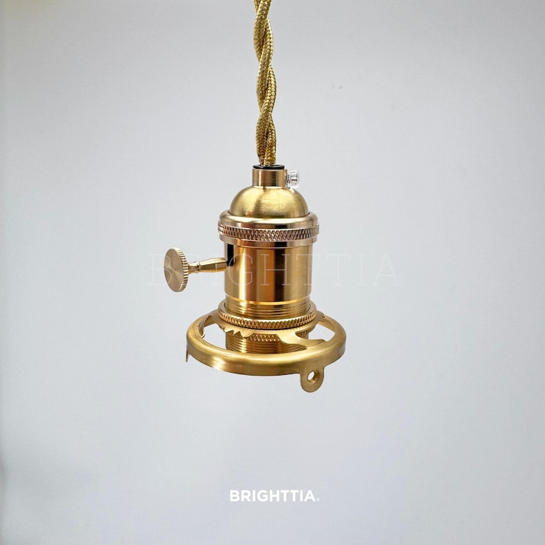 Peut inclure: Une douille de lampe de couleur laiton avec une base d&eacute;corative et un cordon torsad&eacute;. La douille a un petit levier et est con&ccedil;ue pour une ampoule de style Edison. Le mot "BRIGHTTIA" est imprim&eacute; en bas.