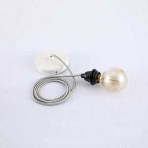 May include: A white ceiling fixture with a black cord and a clear glass light bulb. The cord is coiled and the fixture is attached to the ceiling.