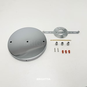 May include: A chrome ceiling rose kit with mounting hardware. The kit includes a circular, polished metal canopy, a mounting bracket, screws, and anchors. The components are arranged on a white surface, ready for installation.