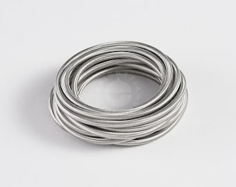 May include: A coiled, silver electrical wire. The wire is tightly wound, forming a circular shape. The image is set against a white background. The word "BRIGHTTIA" is printed at the bottom.