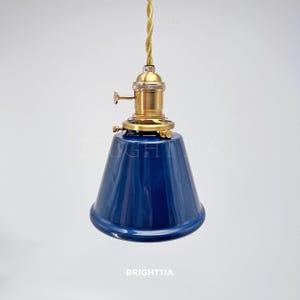 Peut inclure: Suspension luminaire avec abat-jour conique bleu fonc&eacute;. Le luminaire est dot&eacute; d'une douille de couleur laiton et d'un cordon torsad&eacute; dor&eacute;. Le texte "BRIGHTTIA" est visible en bas.