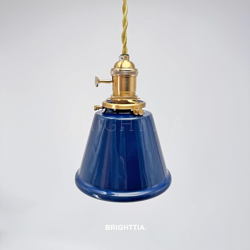 Peut inclure: Suspension luminaire avec abat-jour conique bleu fonc&eacute;. Le luminaire est dot&eacute; d'une douille de couleur laiton et d'un cordon torsad&eacute; dor&eacute;. Le texte "BRIGHTTIA" est visible en bas.