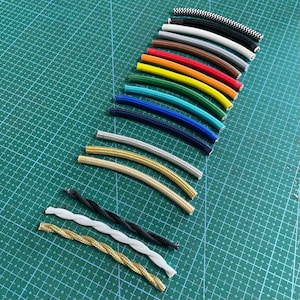 Könnte beinhalten: Eine Auswahl an Stromkabeln in verschiedenen Farben, darunter Schwarz, Weiß, Gold, Silber, Rot, Orange, Gelb, Grün, Blau und Türkis. Die Kabel sind in einem Halbkreis auf einer grünen Schneidematte angeordnet.