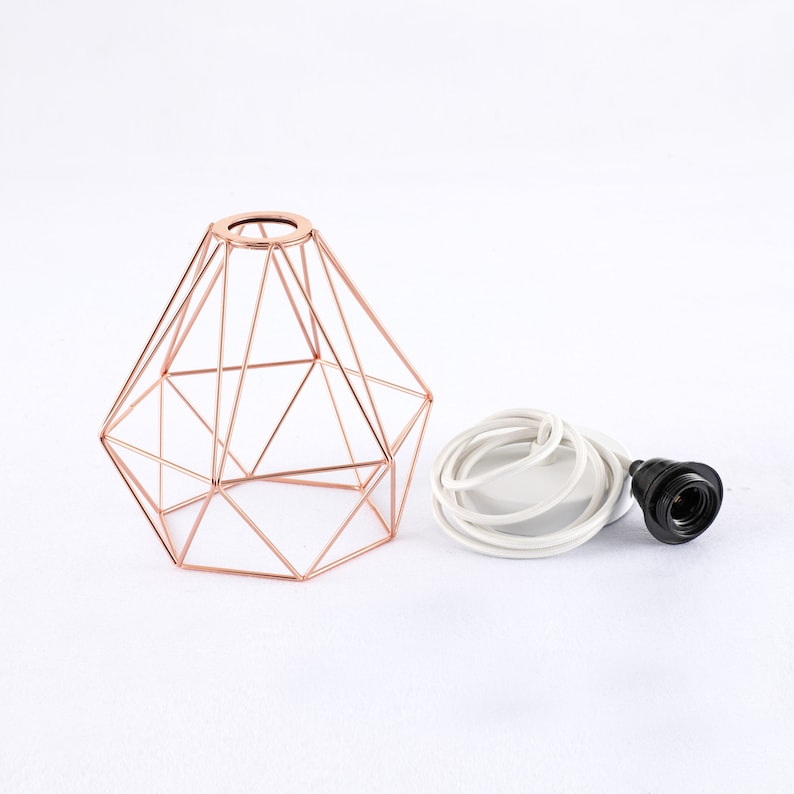 May include: A rose gold geometric wire lampshade with a white cord and black socket.