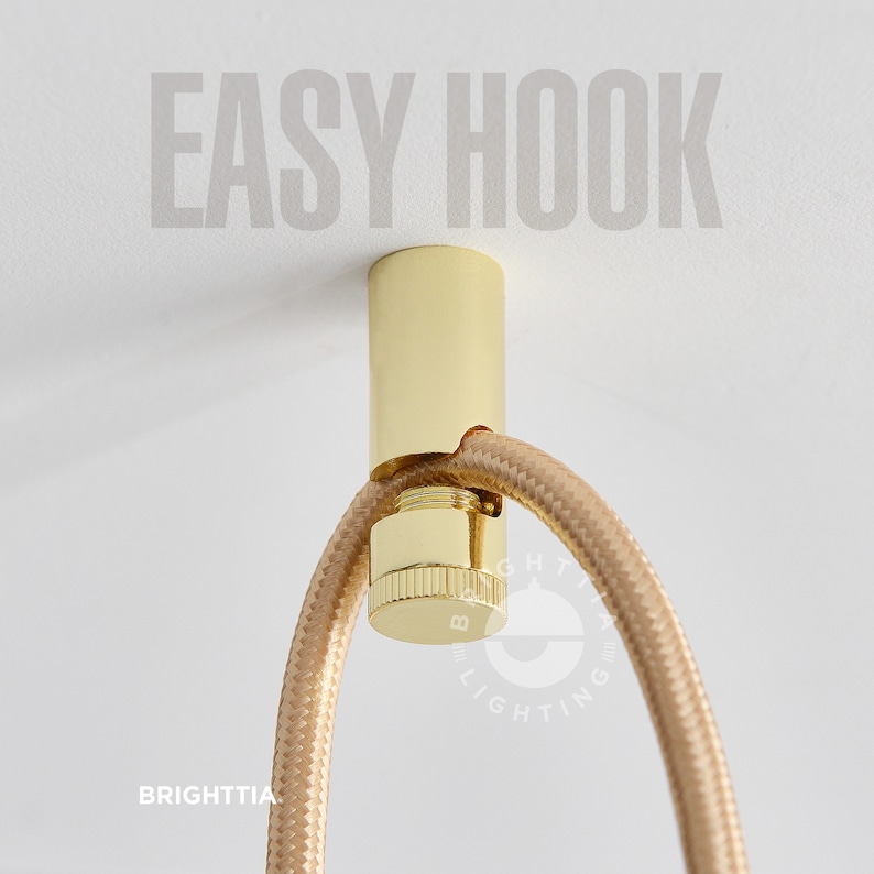 Brighttia Easy Hook in gold mounted on white ceiling with a gold fabric cord hanging on it.