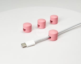 May include: Four pink cable organizers with a white cable running through one of them. The cable organizers are small and round with a hole in the center to hold the cable.