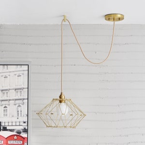 A transformable gold wire shade pendant hung and swag to position on a gold Easy Hook mounted on a white ceiling.