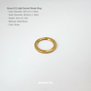 May include: A brass E12 light socket shade ring. The inner diameter is 1.06 inches, the outer diameter is 1.38 inches, and the height is 0.12 inches. The material is solid brass. The text on the image says "BRIGHTTIA."