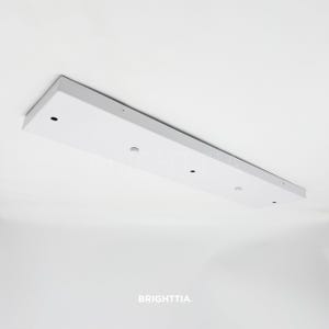 Pode incluir: Uma luminária de teto retangular branca com uma moldura cinza. A luminária tem vários orifícios pequenos e redondos e é montada em um teto branco. A palavra "BRIGHTTIA" é impressa na parte inferior.