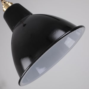 May include: Close-up of a black, glossy, industrial-style pendant light fixture. The interior of the shade is white, and the fixture has a brass-colored accent at the top. The cord is red.