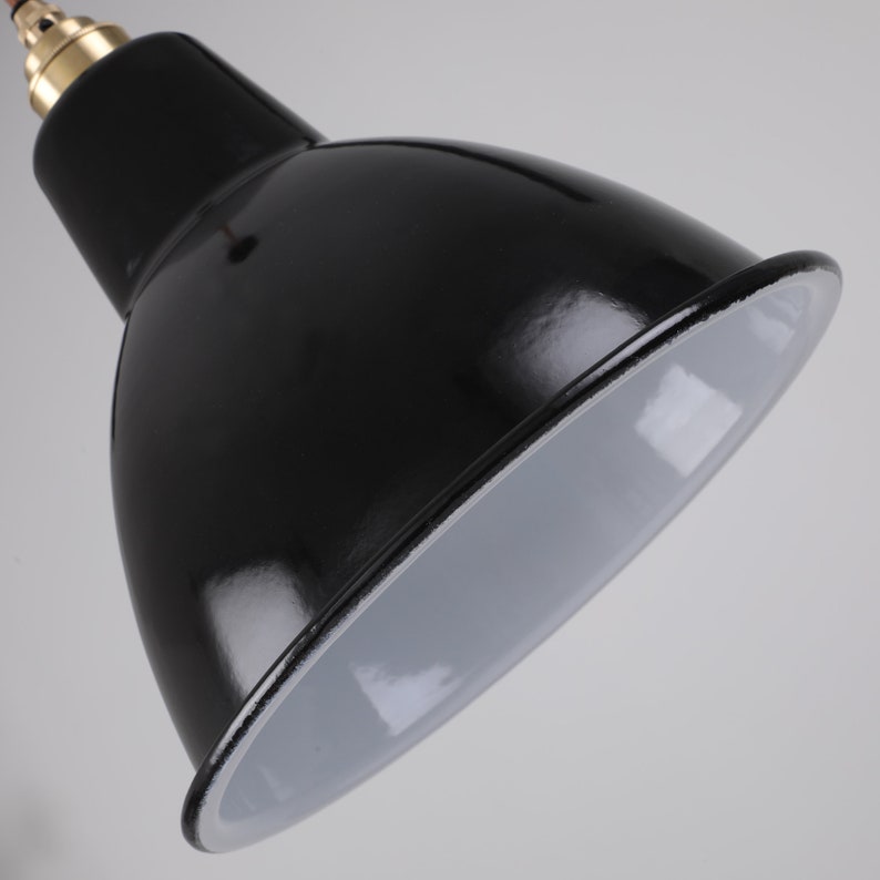May include: Close-up of a black, glossy, industrial-style pendant light fixture. The interior of the shade is white, and the fixture has a brass-colored accent at the top. The cord is red.
