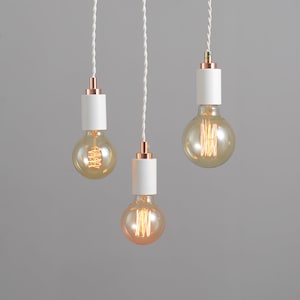 May include: Three white pendant lights with copper accents and clear glass bulbs hanging from white cords against a gray background.