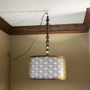 A gold drum shade pendant hung and swag to position on a gold Easy Hook mounted on a white ceiling.