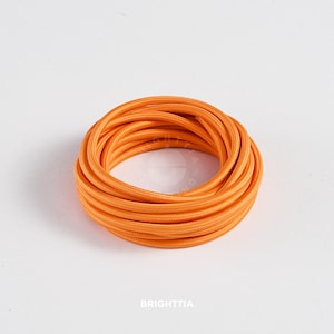 Puede incluir: Primer plano de un cable eléctrico naranja brillante enrollado en una bobina. El cable es liso y tiene una superficie ligeramente texturizada.