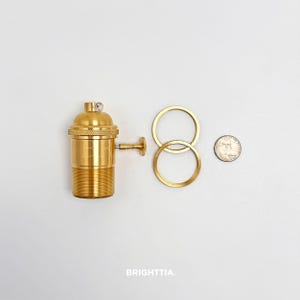 Peut inclure: Un support de lampe en laiton avec une base filet&eacute;e, un petit interrupteur lat&eacute;ral et un dessus d&eacute;coratif. Deux anneaux en laiton et une pi&egrave;ce de monnaie sont &eacute;galement pr&eacute;sents. Le mot "BRIGHTTIA" est imprim&eacute; en bas.