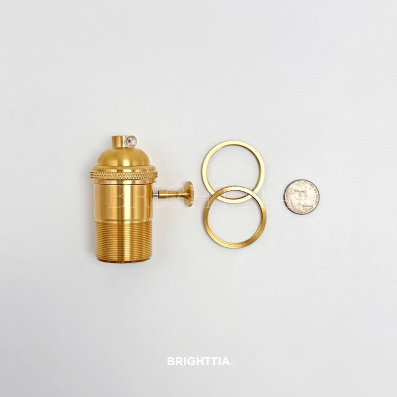 Peut inclure: Un support de lampe en laiton avec une base filet&eacute;e, un petit interrupteur lat&eacute;ral et un dessus d&eacute;coratif. Deux anneaux en laiton et une pi&egrave;ce de monnaie sont &eacute;galement pr&eacute;sents. Le mot "BRIGHTTIA" est imprim&eacute; en bas.