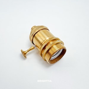 Peut inclure: Une douille de lampe en laiton avec un design textur&eacute; et un petit interrupteur. La douille a une base filet&eacute;e et un petit interrupteur rond. Le mot "BRIGHTTIA" est imprim&eacute; en bas.