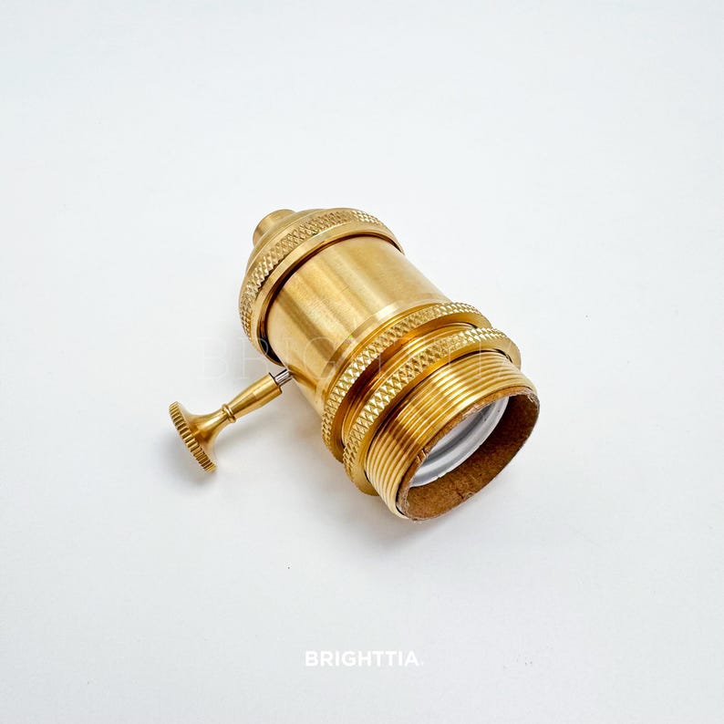 Peut inclure: Une douille de lampe en laiton avec un design textur&eacute; et un petit interrupteur. La douille a une base filet&eacute;e et un petit interrupteur rond. Le mot "BRIGHTTIA" est imprim&eacute; en bas.
